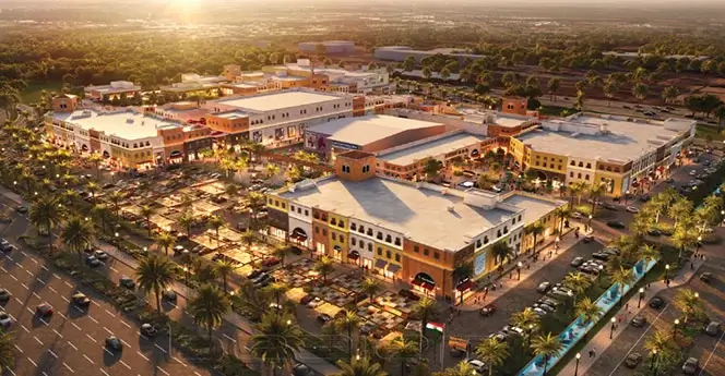 Aerial view of a vibrant mixed-use retail and commercial complex with landscaped plazas, palm-lined streets, and Mediterranean-style architecture at sunset.