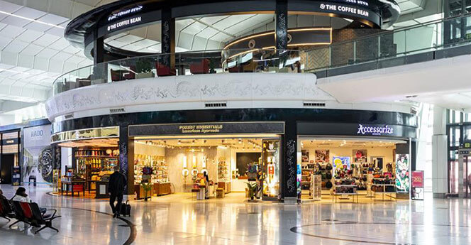 Interior view of an airport shopping area with stores like 'Accessorize' and 'The Coffee Bean' showcasing modern space with a clean, spacious design.