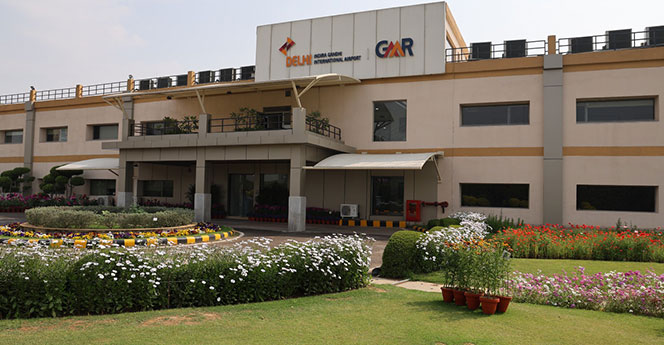 Front view of GMR Delhi Indira Gandhi International Airport support facility with landscaped gardens and signage, showcasing airport infrastructure and operations hub.