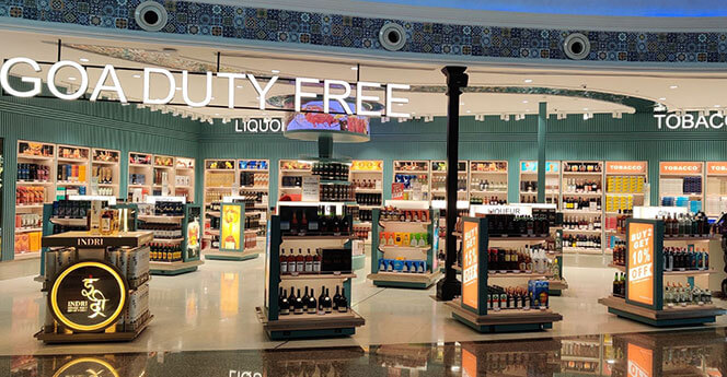 A brightly lit duty-free store at Goa Airport featuring a wide selection of liquor and tobacco products, with organized shelves and promotional signage offering discounts.