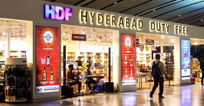 Hyderabad Duty Free store entrance with illuminated signage, advertisements, and a shopper walking by
