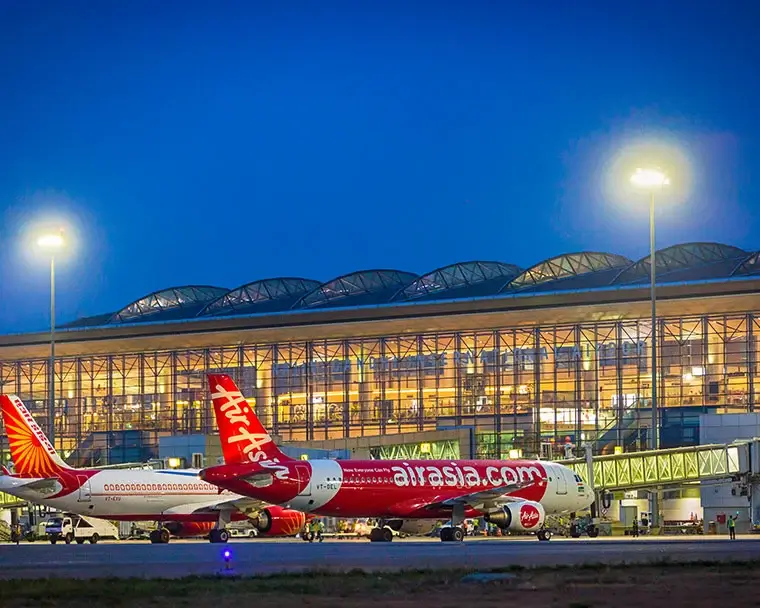 Night view of an airport with Air India and AirAsia planes parked, and the illuminated terminal in the background.