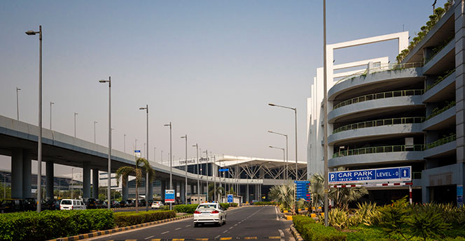 Exterior view of GMR Hyderabad International Airport with elevated roads, parking structure, and terminal entrance, showcasing modern airport infrastructure and passenger access.
