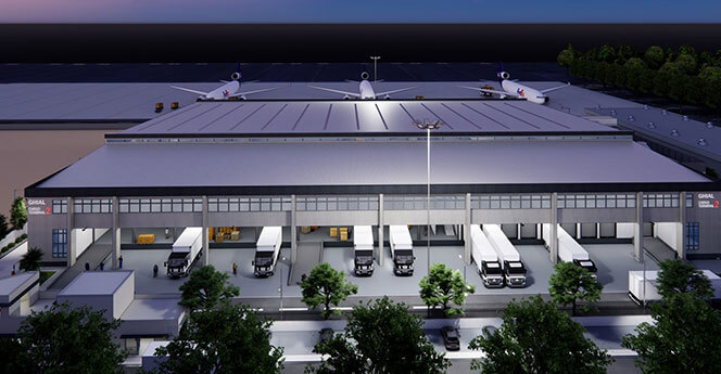 Industrial warehouse with trucks parked at loading docks and large rooftop fans, illuminated at dusk.